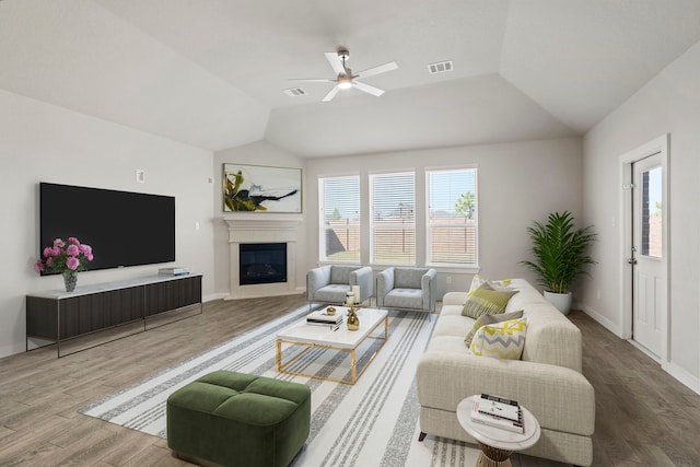 living area featuring visible vents, a glass covered fireplace, ceiling fan, wood finished floors, and vaulted ceiling