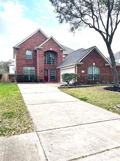 traditional home with brick siding, fence, a garage, driveway, and a front lawn