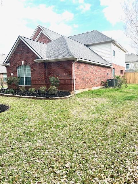 view of home's exterior featuring brick siding, a yard, roof with shingles, central AC, and fence