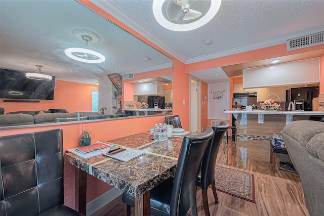 dining area with a textured ceiling, ornamental molding, wood finished floors, and visible vents