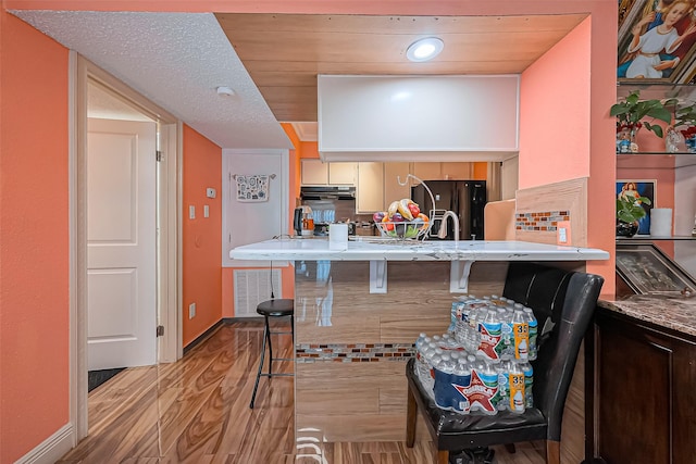 kitchen with light wood finished floors, a breakfast bar area, freestanding refrigerator, under cabinet range hood, and baseboards