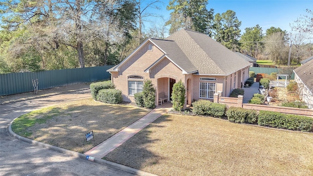 view of front of house featuring roof with shingles, fence, a front lawn, and brick siding