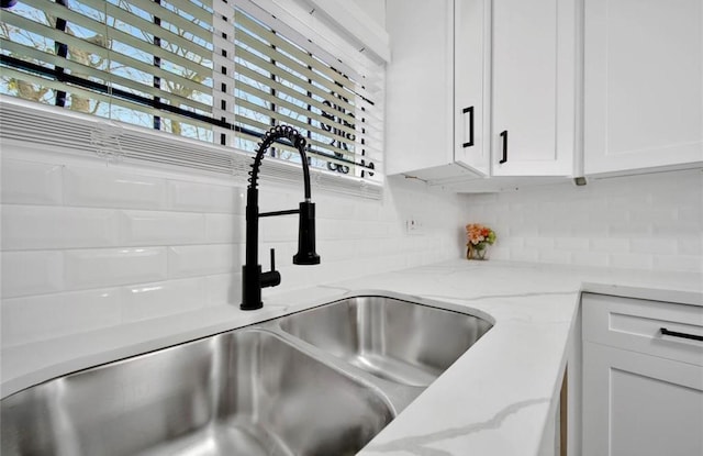 interior details with backsplash, a sink, white cabinetry, and light stone countertops