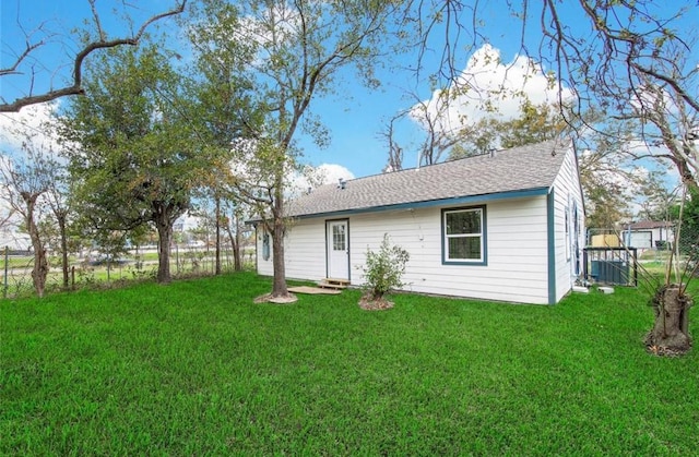 back of house with roof with shingles, a lawn, and fence