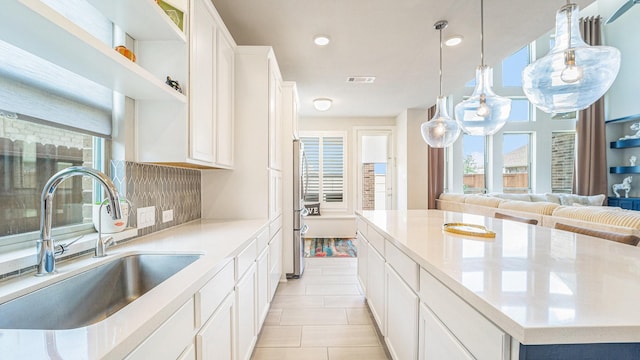 kitchen featuring a spacious island, a sink, visible vents, light countertops, and tasteful backsplash