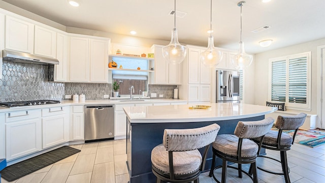 kitchen featuring a kitchen island, stainless steel appliances, light countertops, under cabinet range hood, and a sink