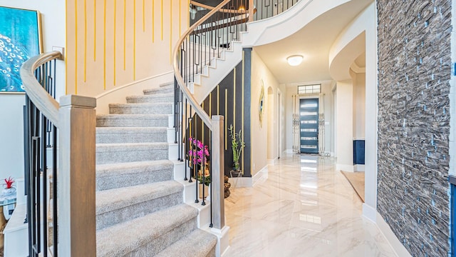 foyer entrance featuring a high ceiling, marble finish floor, stairway, and baseboards