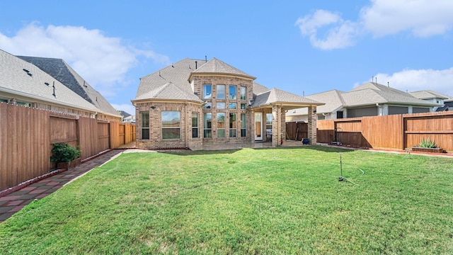 back of house featuring brick siding, a lawn, a shingled roof, and a fenced backyard