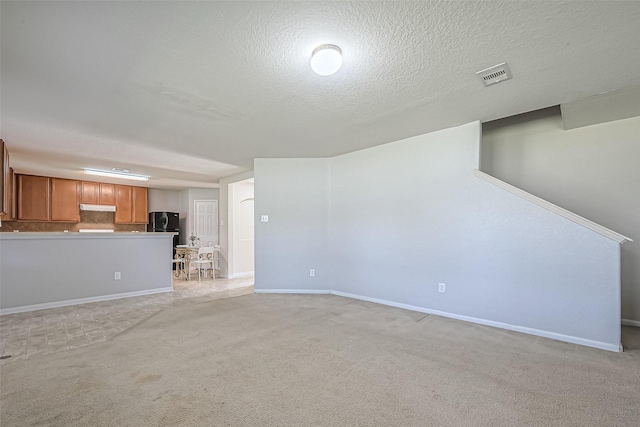 unfurnished living room featuring light carpet, a textured ceiling, visible vents, and baseboards