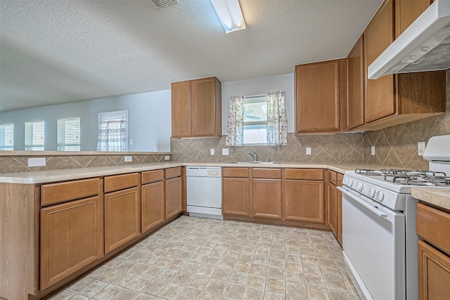 kitchen with white appliances, tasteful backsplash, a peninsula, under cabinet range hood, and a sink