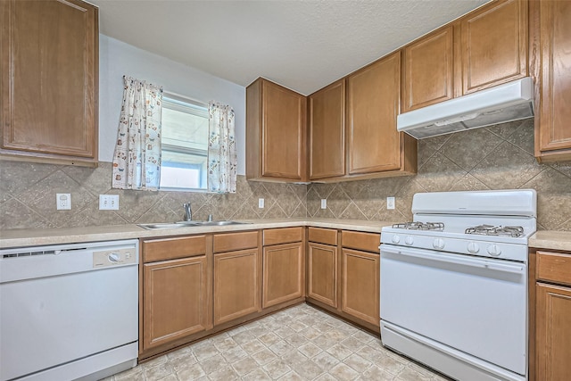 kitchen with white appliances, decorative backsplash, light countertops, under cabinet range hood, and a sink