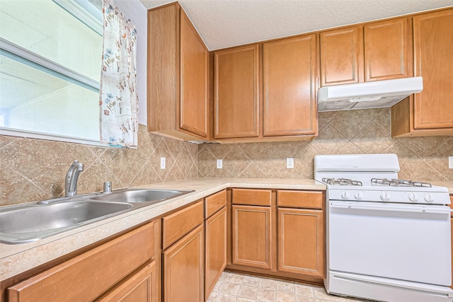 kitchen with under cabinet range hood, a sink, white range with gas cooktop, light countertops, and backsplash