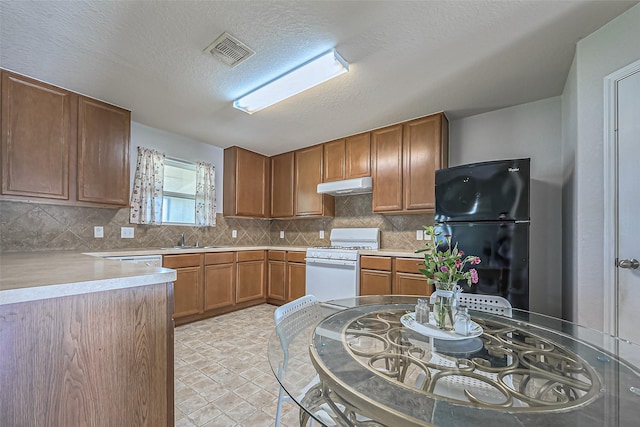 kitchen with white range with gas stovetop, visible vents, decorative backsplash, freestanding refrigerator, and under cabinet range hood