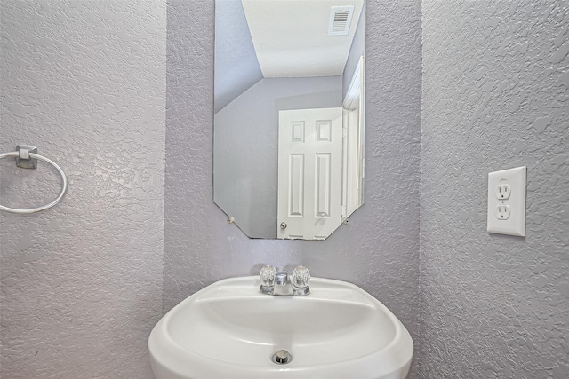 bathroom featuring vaulted ceiling, visible vents, a textured wall, and a sink