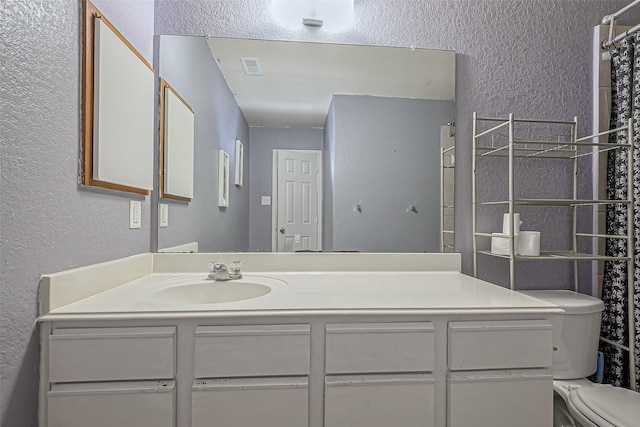 bathroom with visible vents, a textured wall, vanity, and toilet