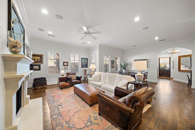 living room featuring arched walkways, a fireplace with raised hearth, dark wood-style flooring, crown molding, and recessed lighting