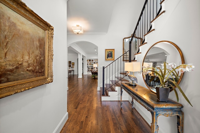 entryway featuring wood finished floors, baseboards, arched walkways, stairs, and crown molding