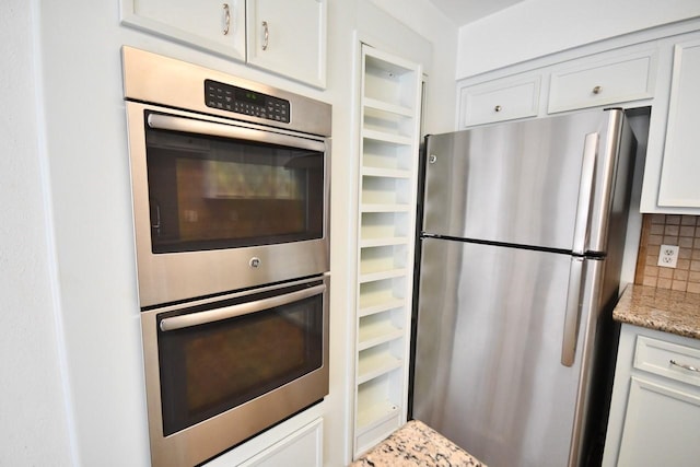 kitchen featuring light stone countertops, appliances with stainless steel finishes, white cabinets, and backsplash