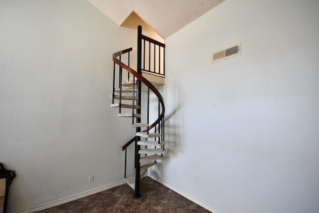 stairway with baseboards, visible vents, lofted ceiling, stone finish floor, and a textured ceiling