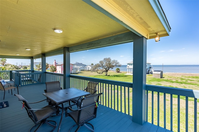 deck featuring outdoor dining area, a water view, and a yard