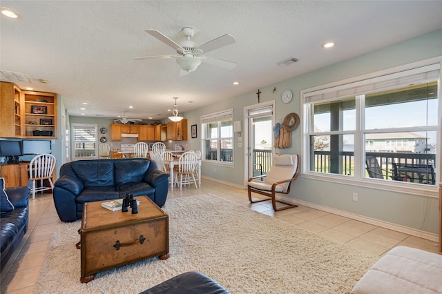 living room with a ceiling fan, visible vents, light tile patterned flooring, and a textured ceiling