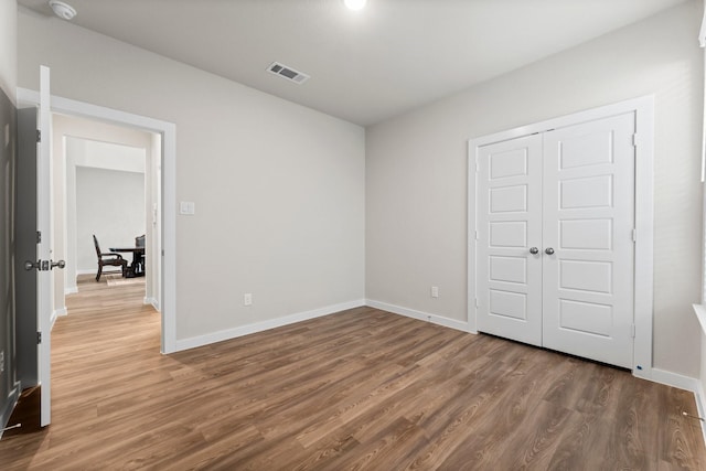 unfurnished bedroom featuring a closet, wood finished floors, visible vents, and baseboards