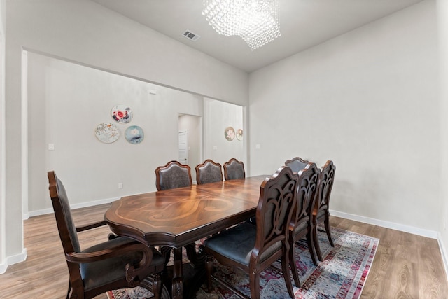 dining space featuring baseboards, wood finished floors, visible vents, and a notable chandelier