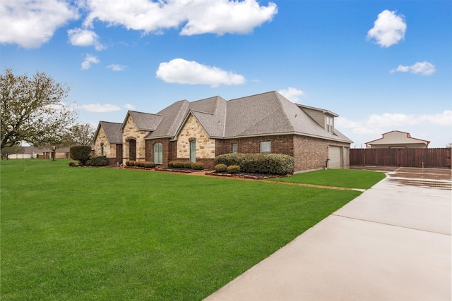 french country home featuring brick siding, fence, concrete driveway, and a front yard