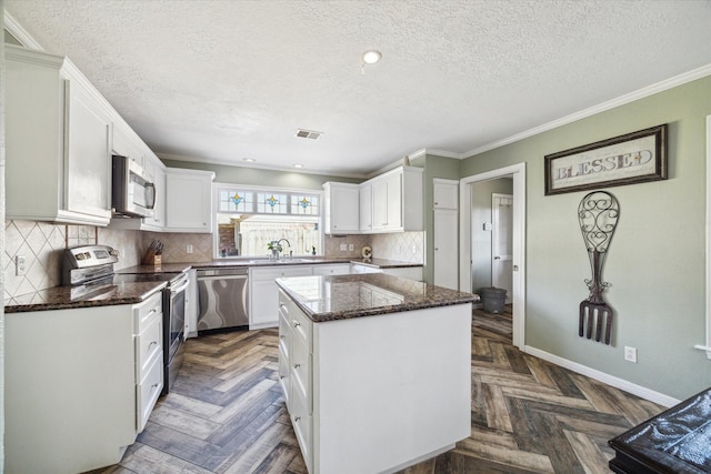 5502 Enchanted Timbers Dr, Humble, TX 77346 - kitchen with appliances with stainless steel finishes, a textured ceiling, a kitchen island, white cabinetry, and dark stone countertops