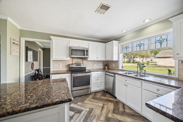 5502 Enchanted Timbers Dr, Humble, TX 77346 - kitchen with appliances with stainless steel finishes, a sink, white cabinets, ornamental molding, and tasteful backsplash