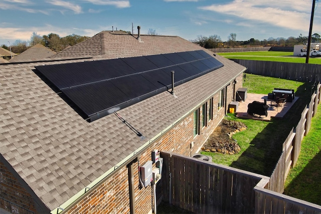 view of home's exterior with solar panels, a shingled roof, a lawn, a patio area, and a fenced backyard