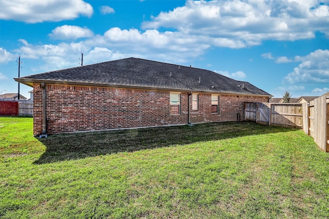 back of house featuring a yard, brick siding, and a fenced backyard