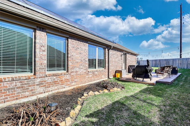 exterior space featuring brick siding, fence, a yard, roof mounted solar panels, and a patio area