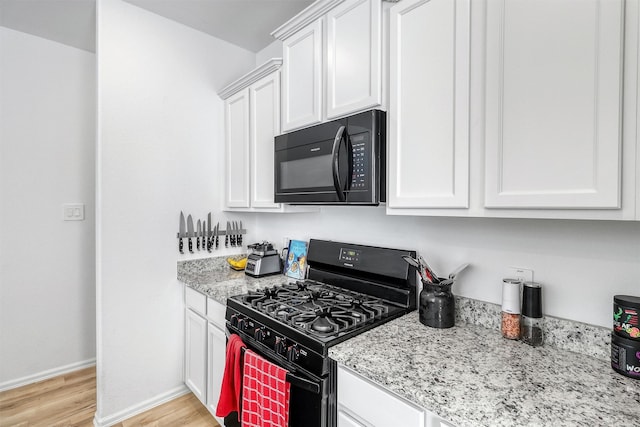 kitchen featuring black appliances, light wood-type flooring, white cabinetry, and light stone countertops