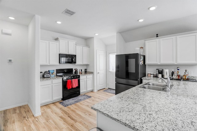 kitchen featuring visible vents, light wood-style floors, white cabinetry, a sink, and black appliances