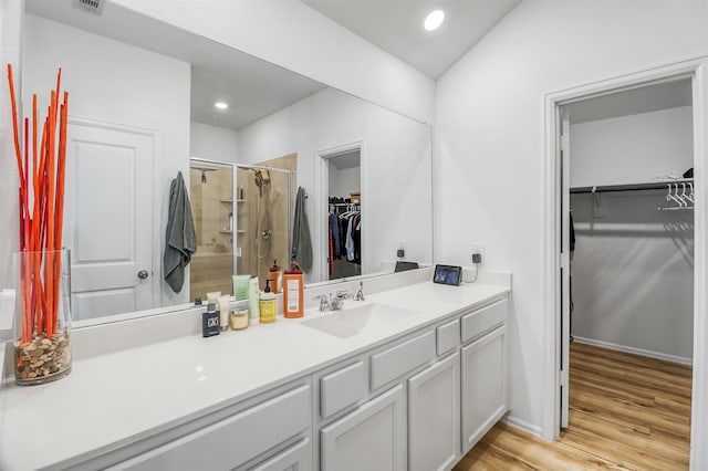 bathroom with recessed lighting, wood finished floors, vanity, a shower stall, and a walk in closet