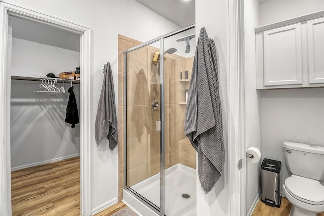 bathroom featuring a stall shower, baseboards, toilet, wood finished floors, and a walk in closet