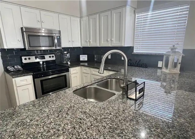 kitchen with stainless steel appliances, tasteful backsplash, white cabinets, a sink, and dark stone counters