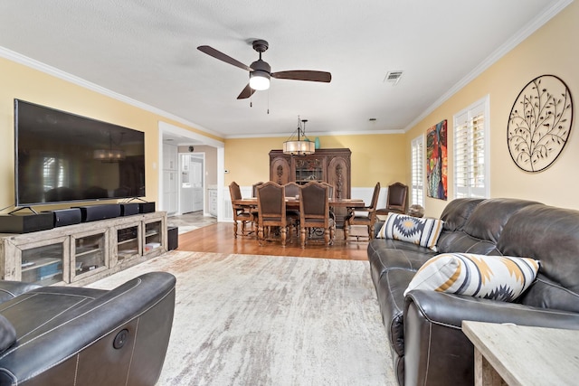 living area featuring a ceiling fan, visible vents, wood finished floors, and ornamental molding