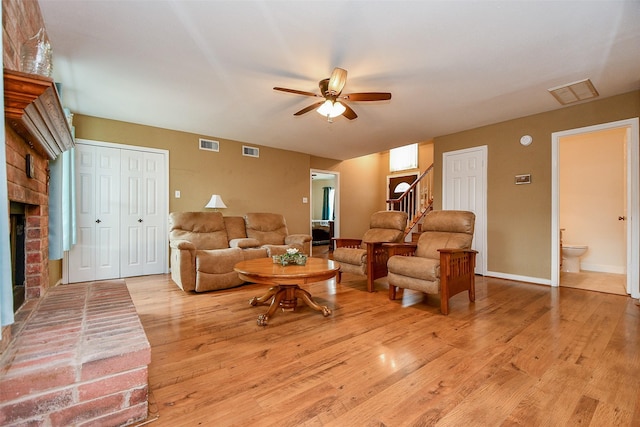 living room featuring a brick fireplace, visible vents, hardwood / wood-style floors, and stairs