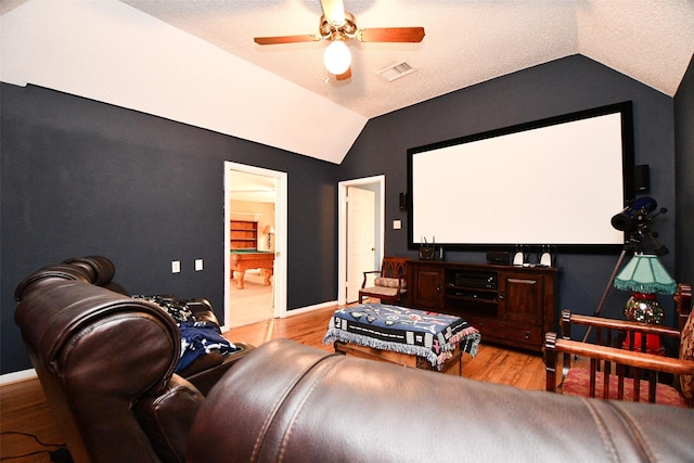 cinema room with visible vents, baseboards, a ceiling fan, light wood-style flooring, and vaulted ceiling