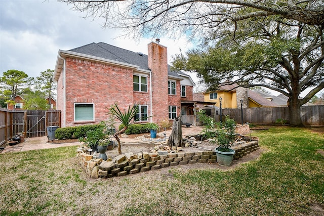 rear view of property with a patio, a fenced backyard, brick siding, a yard, and a chimney