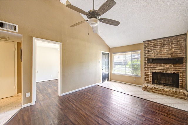 unfurnished living room with visible vents, a brick fireplace, ceiling fan, a textured ceiling, and wood finished floors