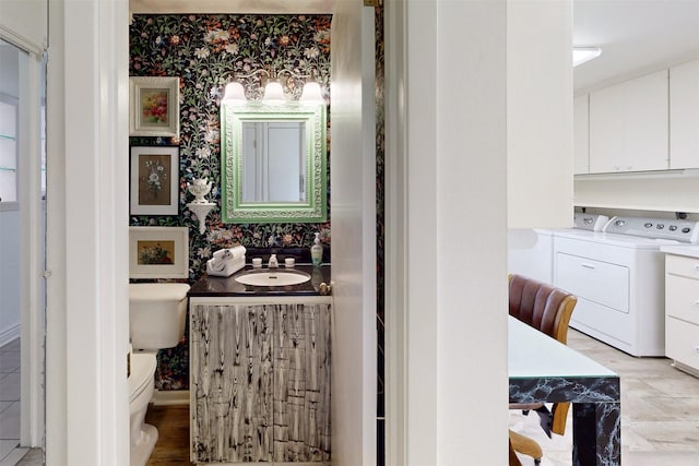 bathroom with toilet, wallpapered walls, a sink, and independent washer and dryer