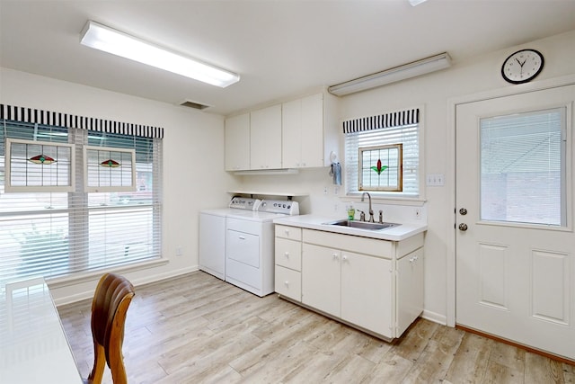 clothes washing area with light wood-style flooring, a sink, visible vents, cabinet space, and washer and clothes dryer