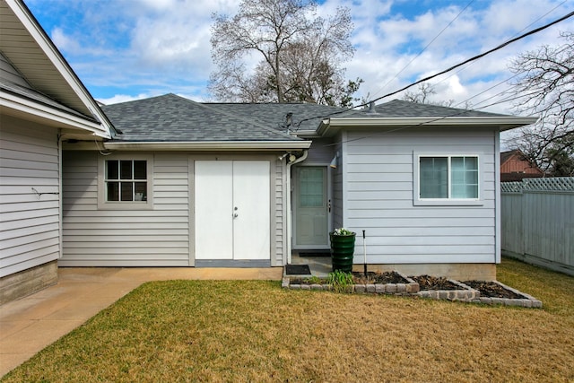 property entrance with roof with shingles, fence, and a yard