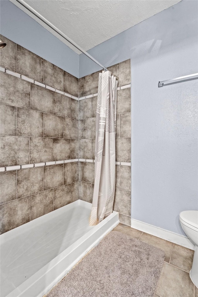 full bathroom with toilet, a tile shower, a textured ceiling, baseboards, and tile patterned floors