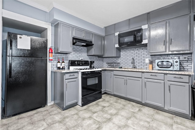 kitchen featuring gray cabinetry, under cabinet range hood, a sink, black appliances, and tasteful backsplash