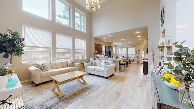 living room with recessed lighting, a towering ceiling, baseboards, light wood finished floors, and an inviting chandelier