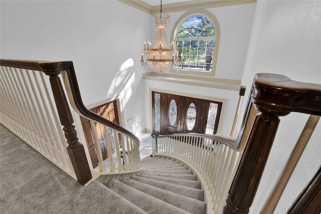 stairway with a towering ceiling, an inviting chandelier, carpet, and crown molding